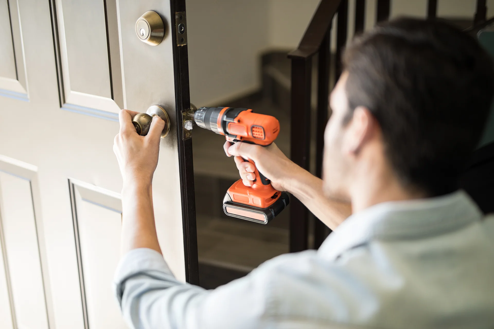 A person using a cordless drill to install a handle on a dark door.