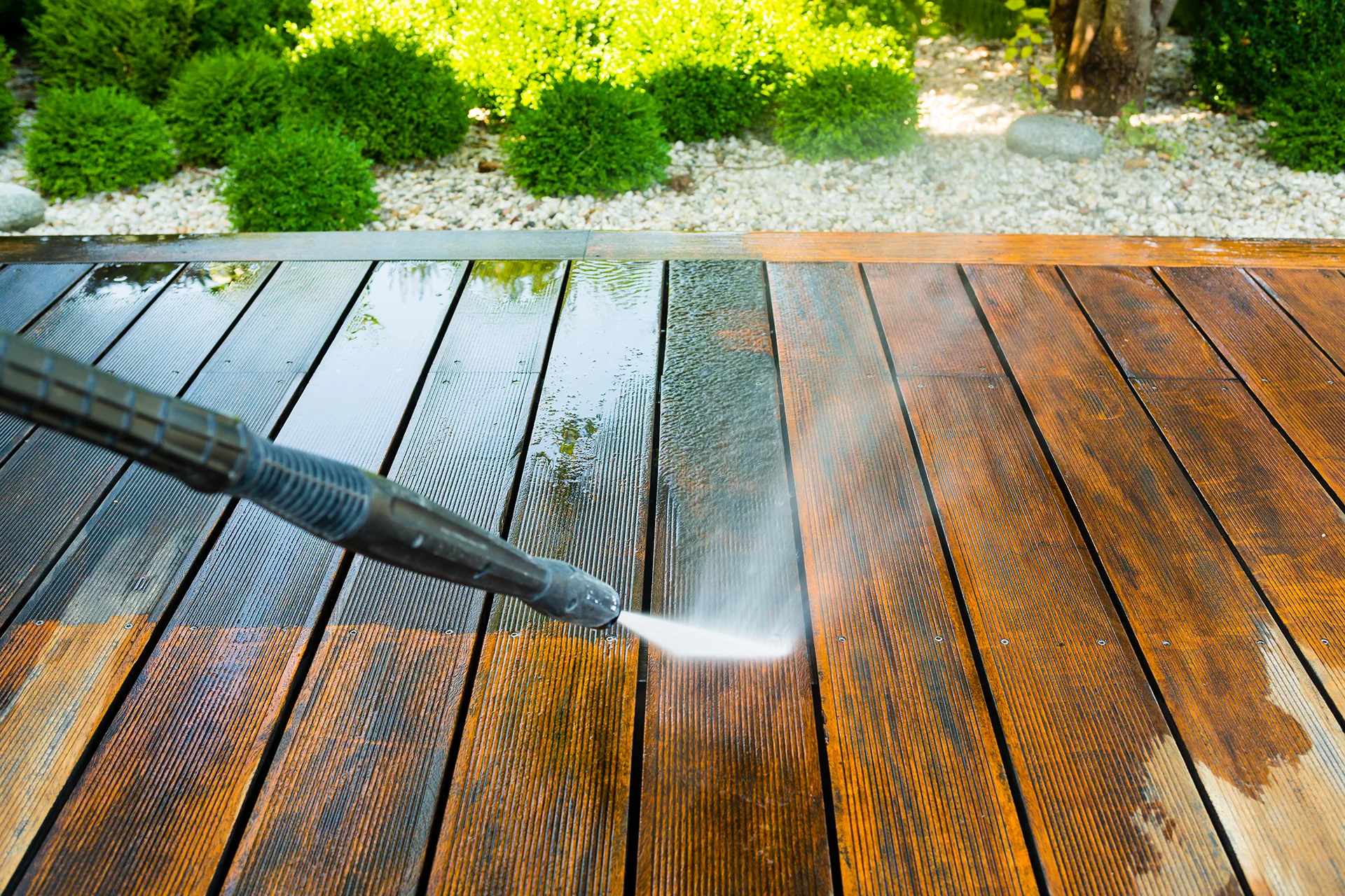 A pressure washer spraying water to clean a wooden deck outdoors.